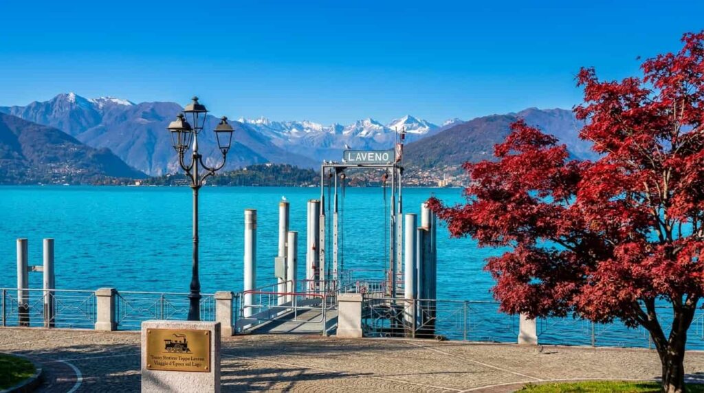 Vista panoramica del lungolago di Laveno Mombello sul Lago Maggiore con l'imbarcadero e le montagne, meta del viaggio con il Treno Storico Trenord.